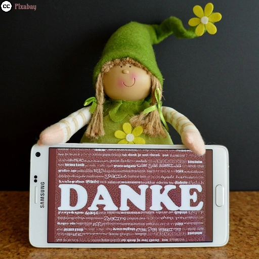 Eine grün angezogene Wichtelfigur hält ein Smartphone, auf dem &bdquo;DANKE&rdquo; zu lesen ist.
