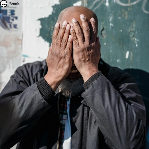 Ein Mensch verbirgt sein Gesicht hinter beiden Händen und steht vor einer verwitterten Wand – Sinnbild für Überforderung und verlorene Orientierung.