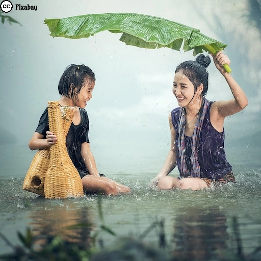 Zwei asiatische Frauen sitzen lachend im Regen und sch&uuml;tzen sich mit einem großen Blatt. Dieses Foto symbolisiert ein naturnahes und unbeschwertes Leben.