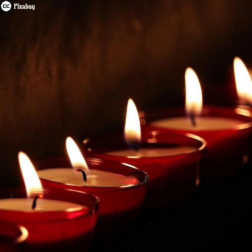 Mehrere Grablichter brennen in einer dunklen Umgebung und spenden warmes Licht.