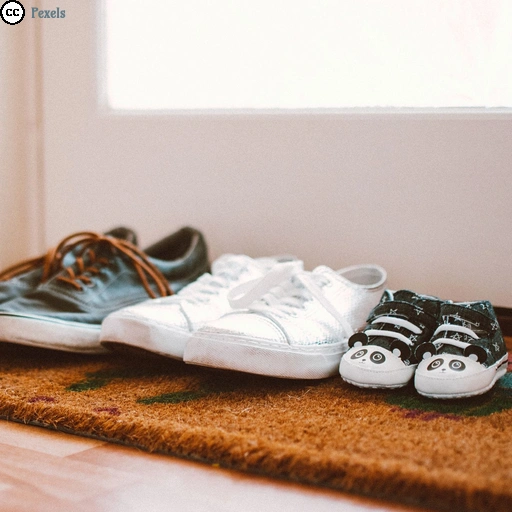 Auf einer Fußmatte vor einer weißen Tür stehen drei unterschiedliche Paar Schuhe.