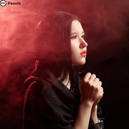 Eine junge Frau scheint zu beten. Rotes Licht und Rauchschwaden. Foto von Mikhail Nilov auf Pexels.